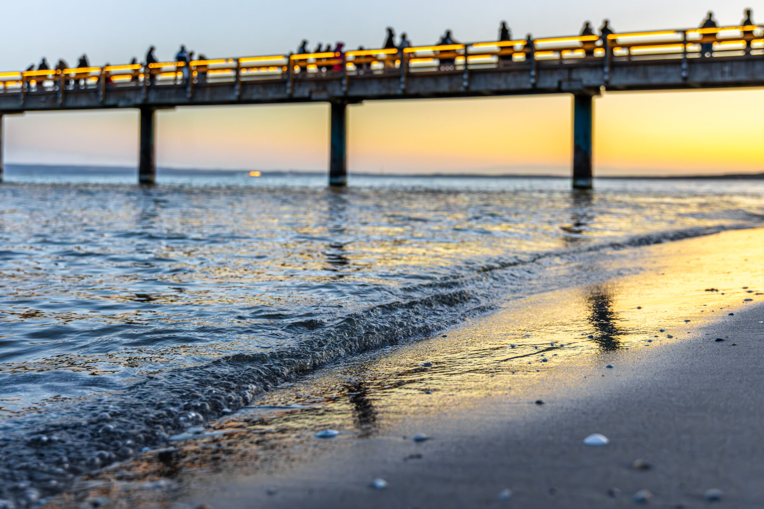 Evening pier over sea waves at sunset with people walking on boardwalk golden hour Atlantic City